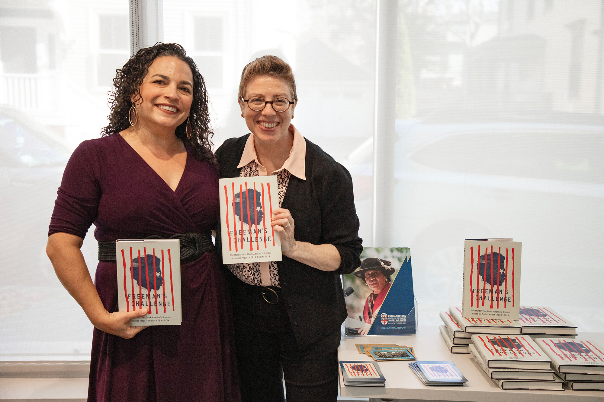 Two people standing and holding a book whilst smiling.