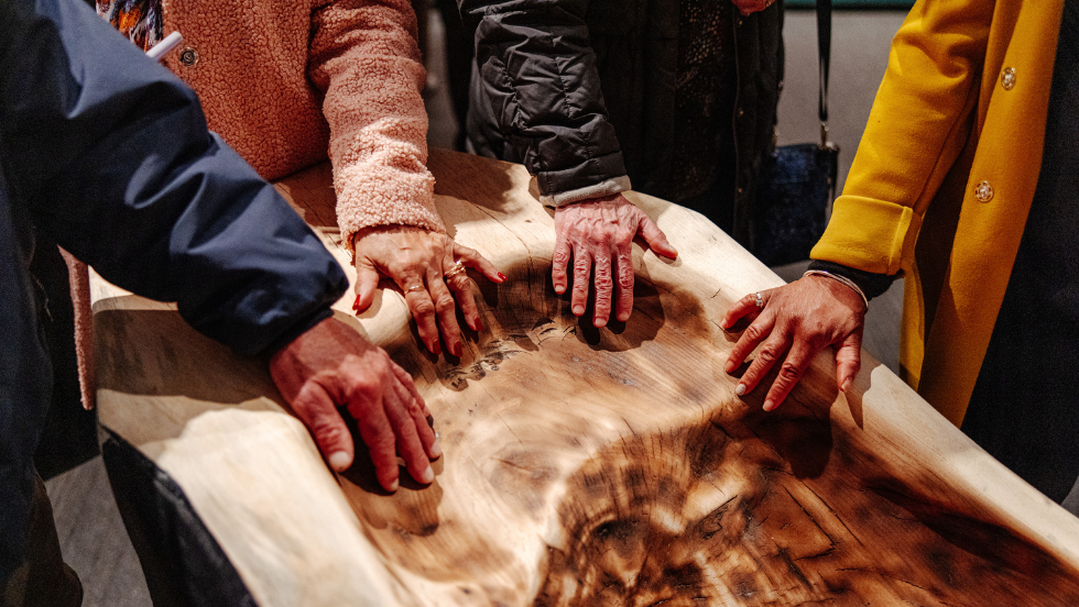 Five hands touch the muhshoon dugout canoe.