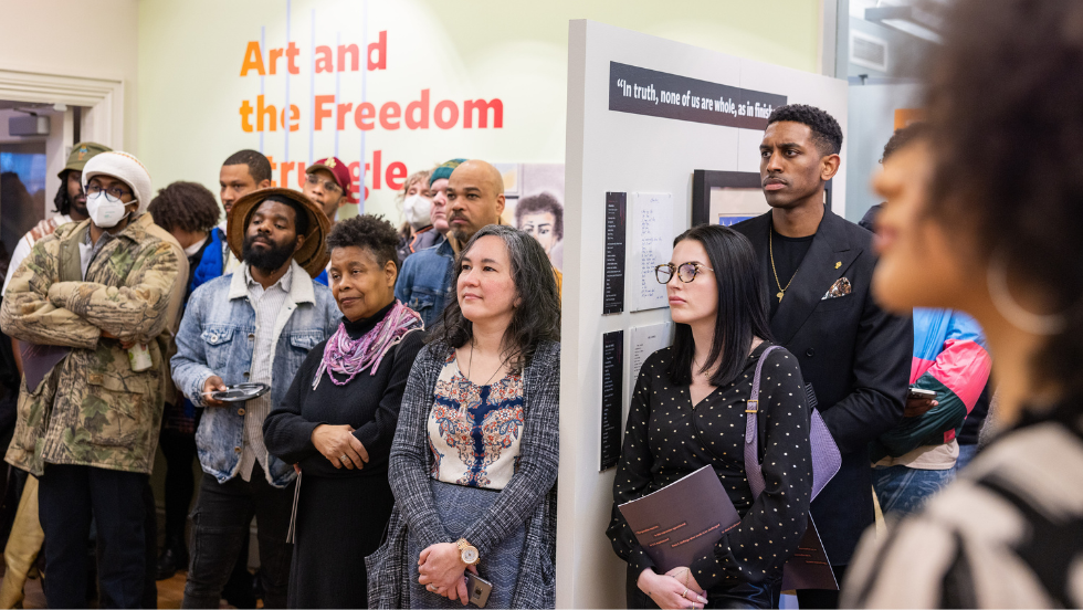 Marcus Grant and exhibition opening visitors watch the premiere of "Panther Walk," lyrics and music by Mumia Abu-Jamal.