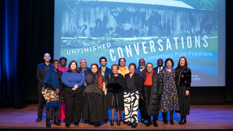 Contributors to the Brown-led "Unfinished Conversations" oral history project pose for an image in front of a projector screen reading, "Unfinished Conversations Documentary Film Premiere."