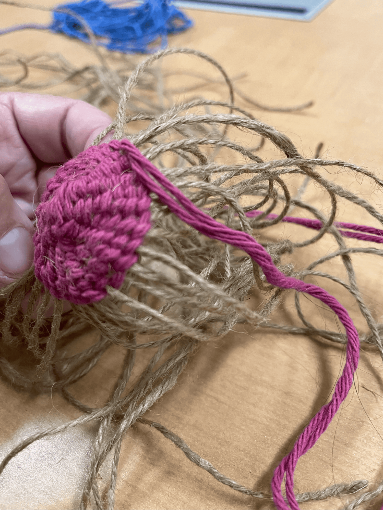 A hand holding twine and pink yarn being woven into a basket