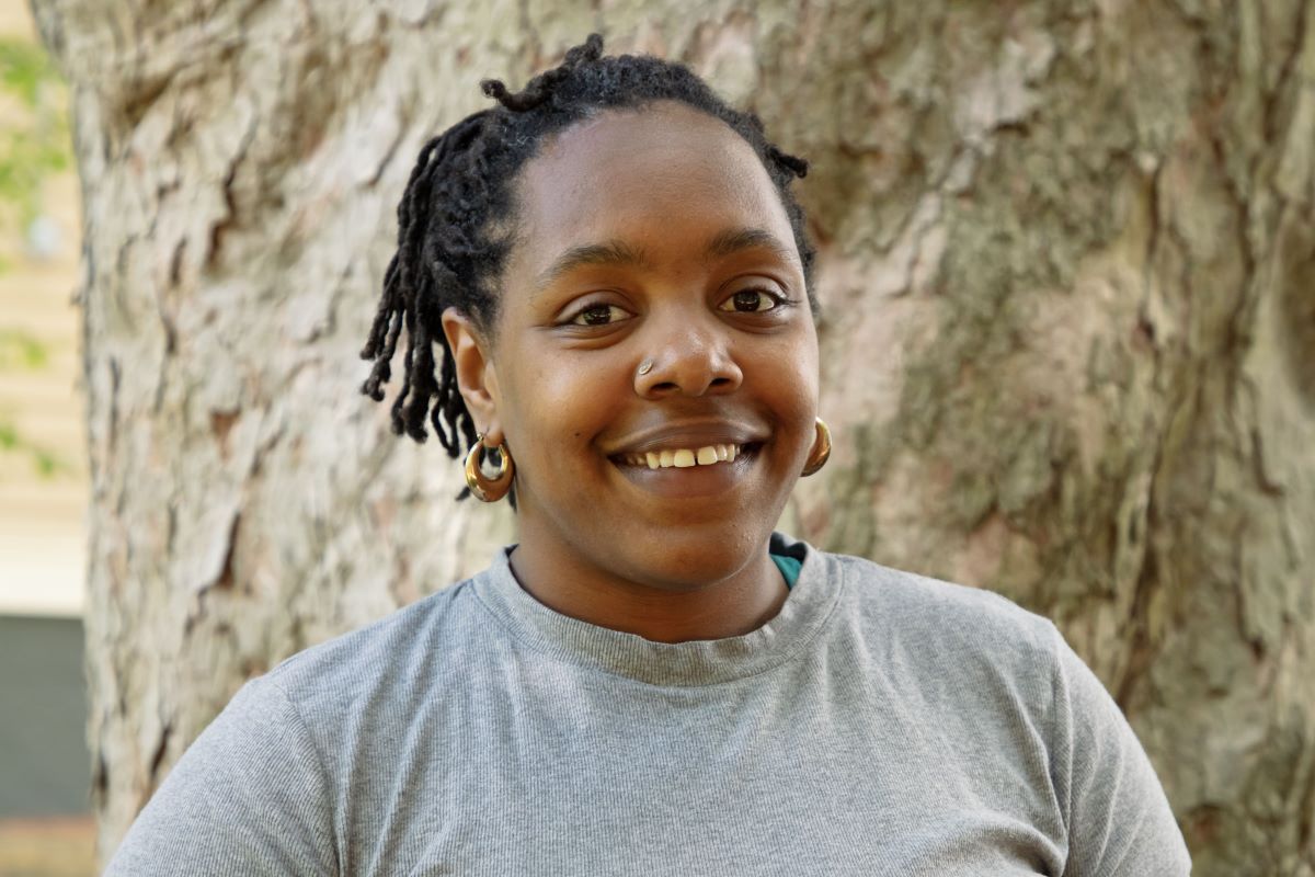 Reina Thomas smiles at the camera standing in front of a tree trunk