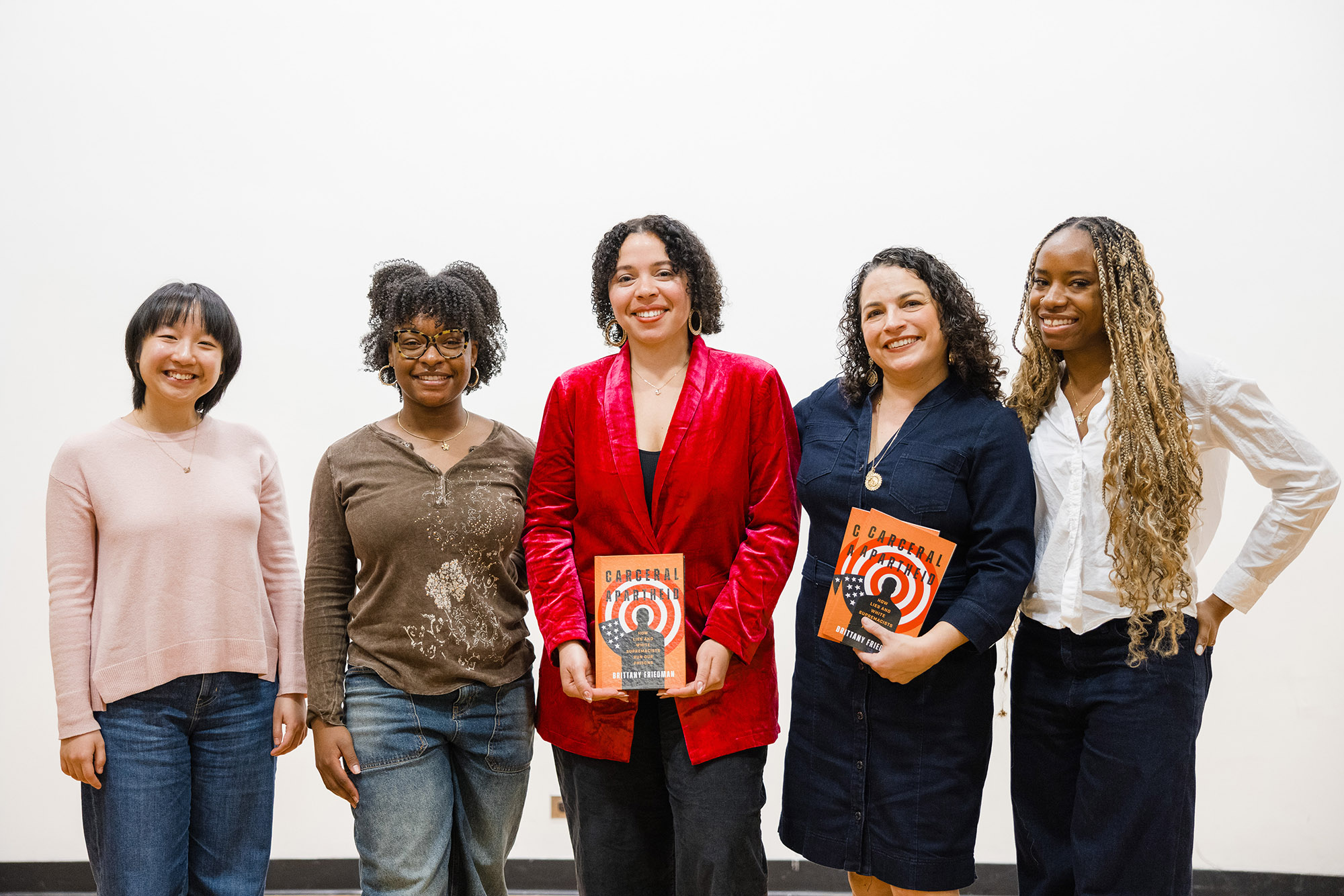 Three students stand with a professor and an author whose book they're holding