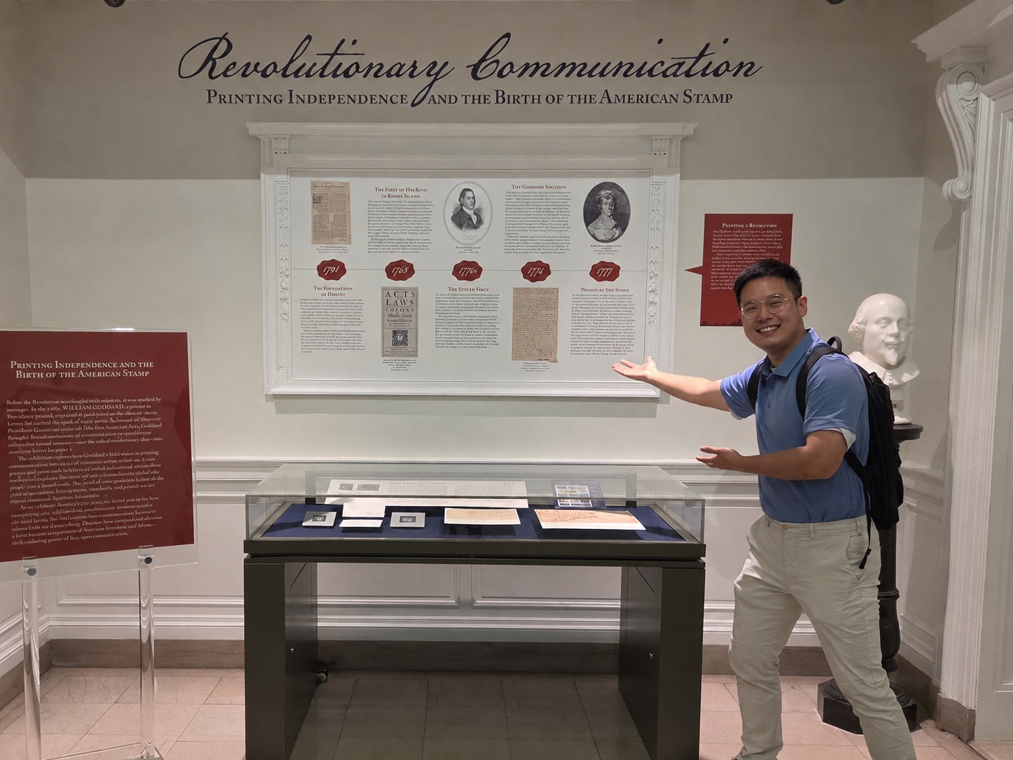 Ray Zhang standing in an exhibition of historic documents and gesturing toward the display while smiling