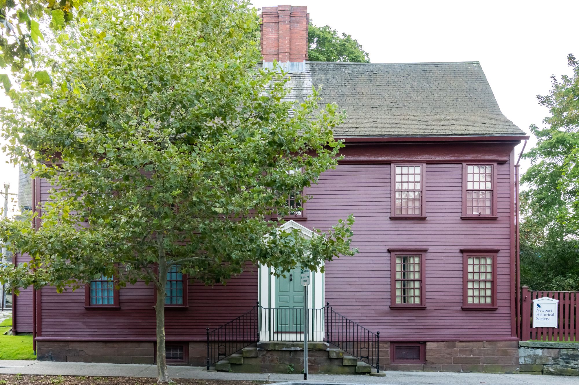 A dark red cape-style colonial building with a tree