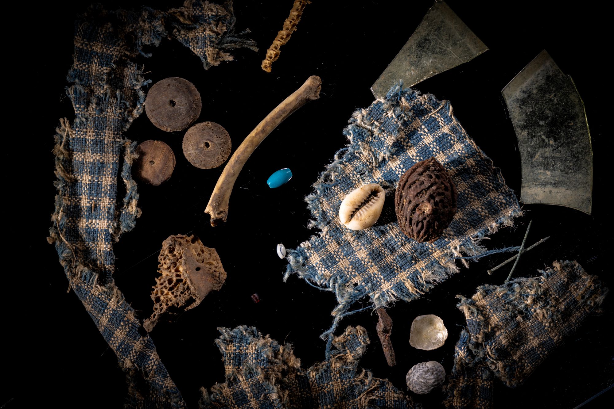 a collection of small items including scraps of blue and white checkered fabric, bones, a cowrie shell, buttons and beads