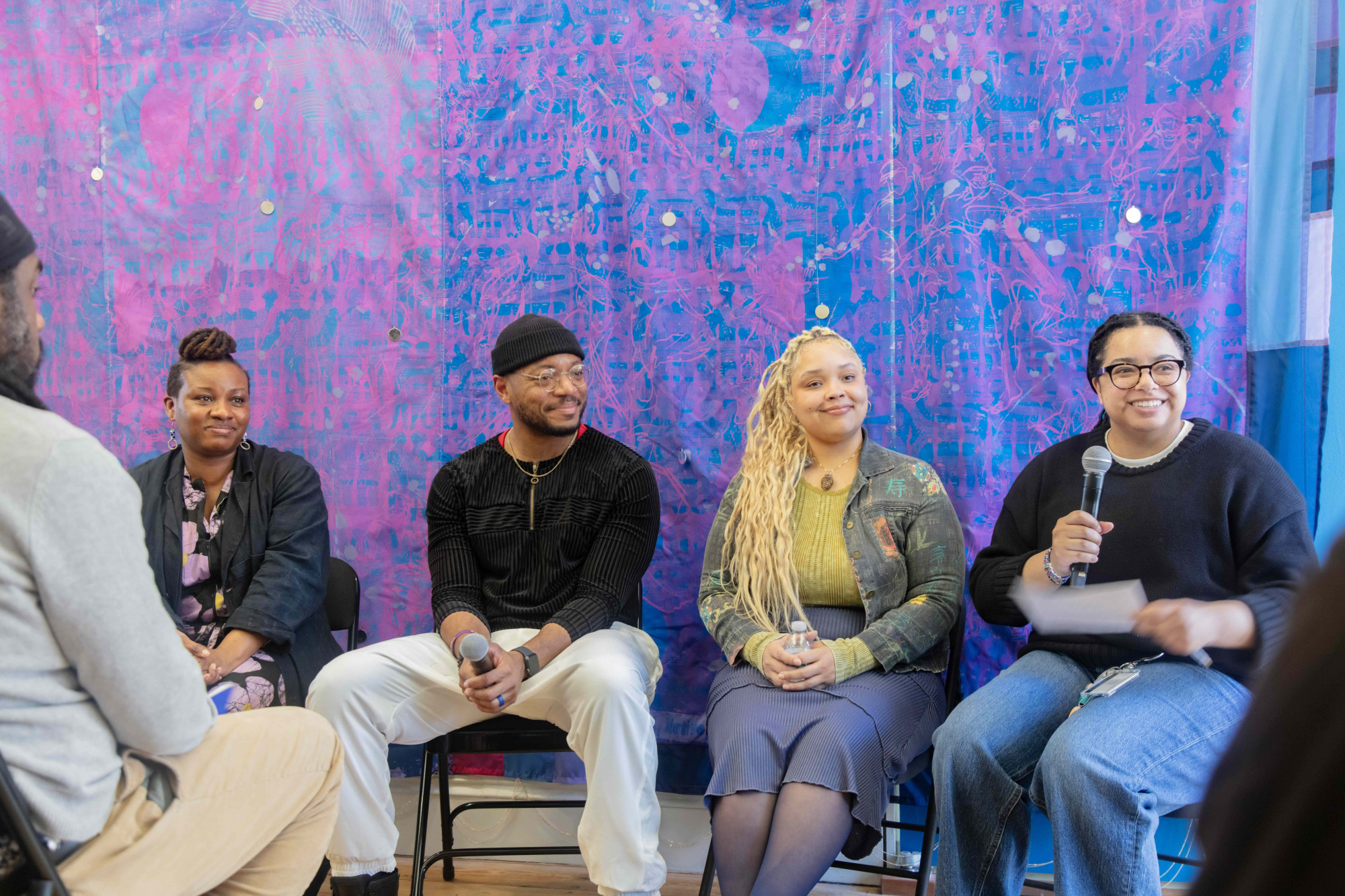 A group of people seated in front of a colorful fabric panel.