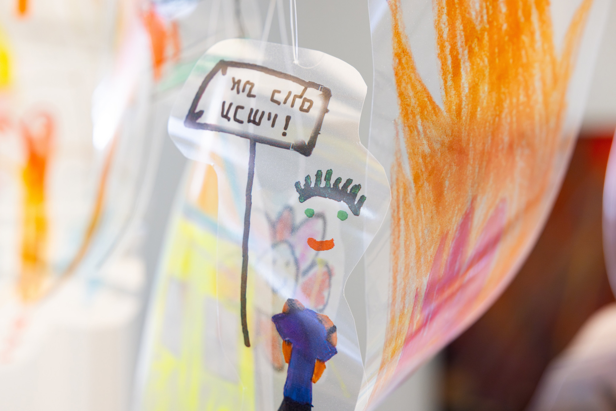 A hanging children's drawing of a person holding a sign on translucent plastic as part of the Innocent Knowledge Exhibition