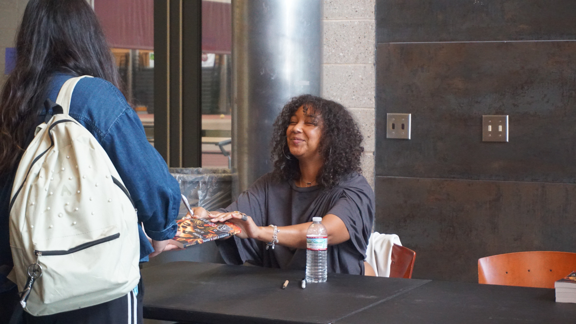A woman smiling and handing a signed book to another person.