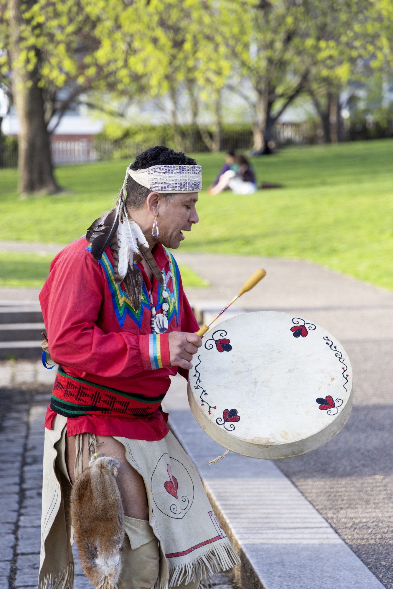 A man dressed in Indigenous clothing while playing a native drum.