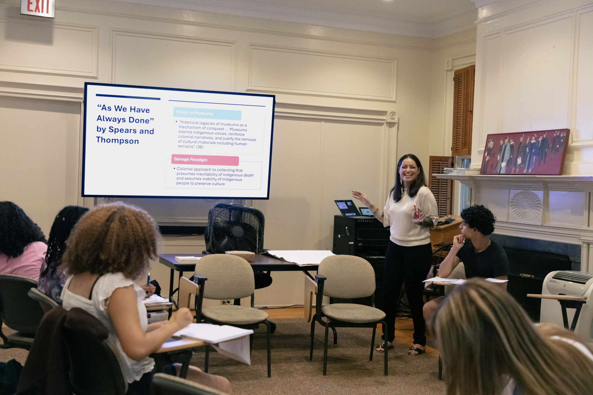 A woman standing at the front of a room lecturing a circle of students