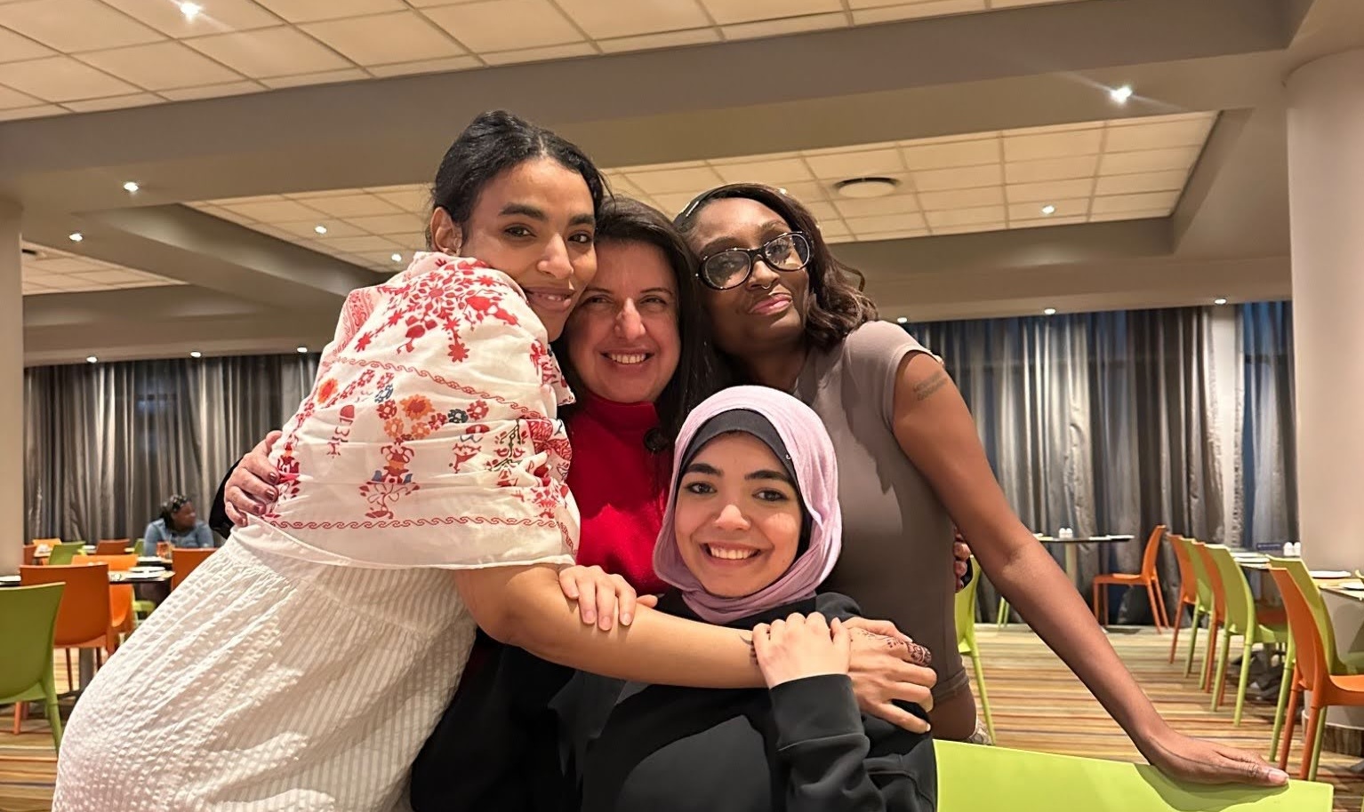 Group of four people hugging one another while smiling to the camera.