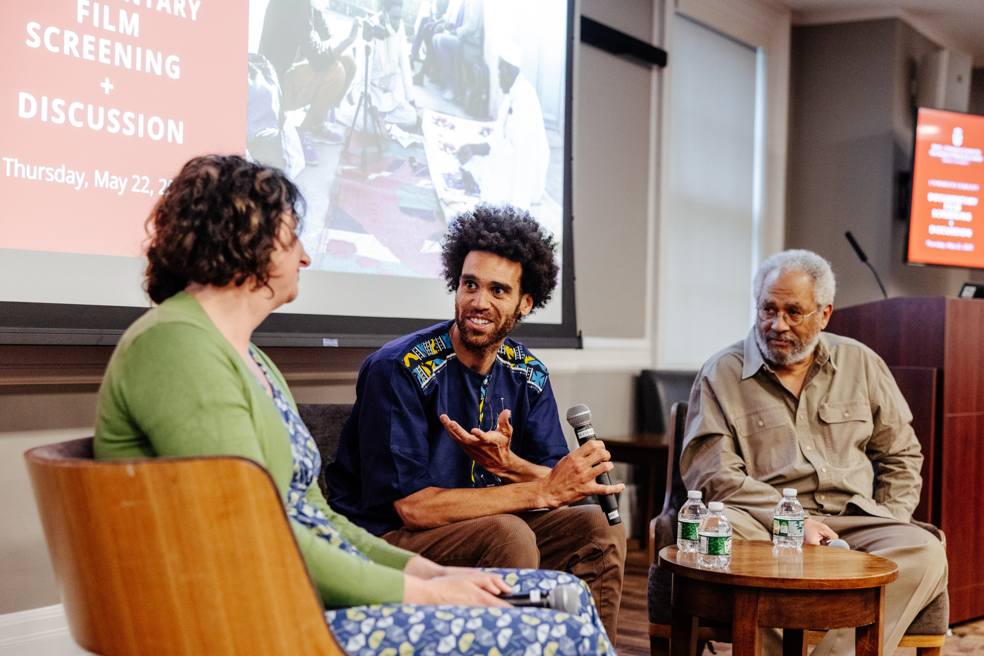 Three seated people with microphones talking.