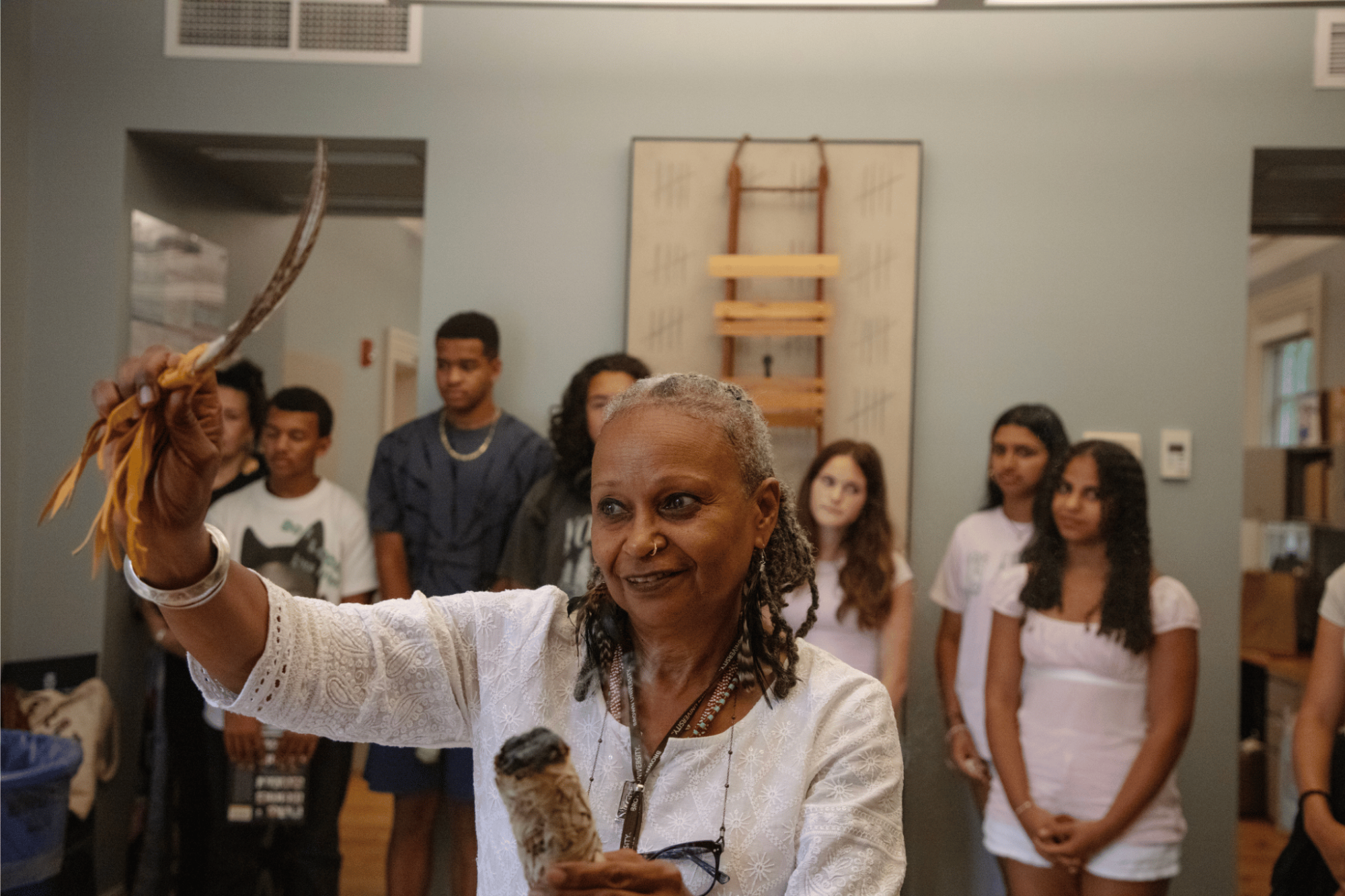 Woman holding a feather and sage smudge with students in the background