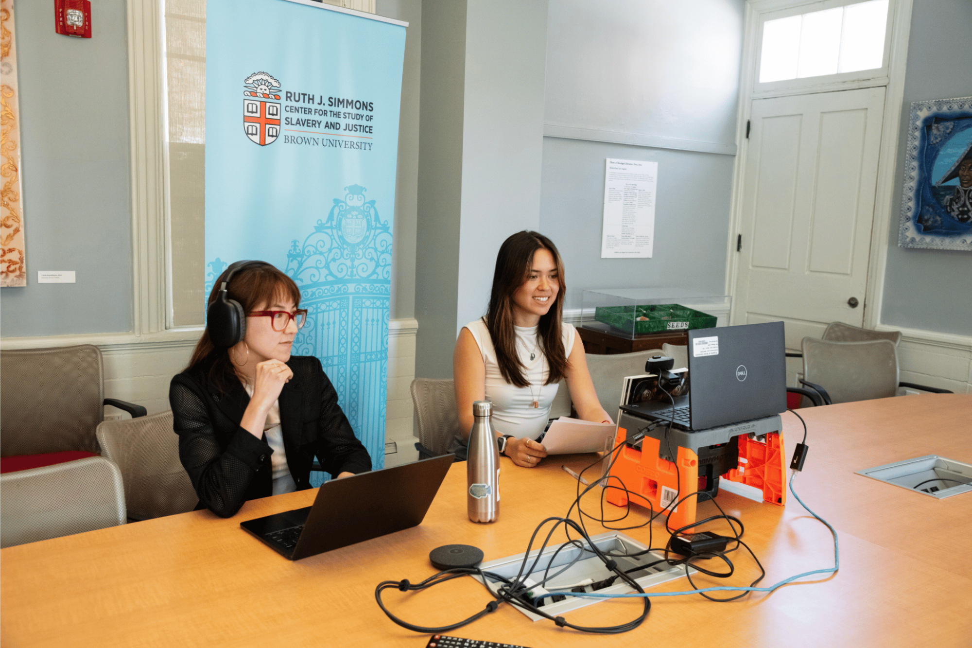 Two women sitting at a table at laptops on a video call
