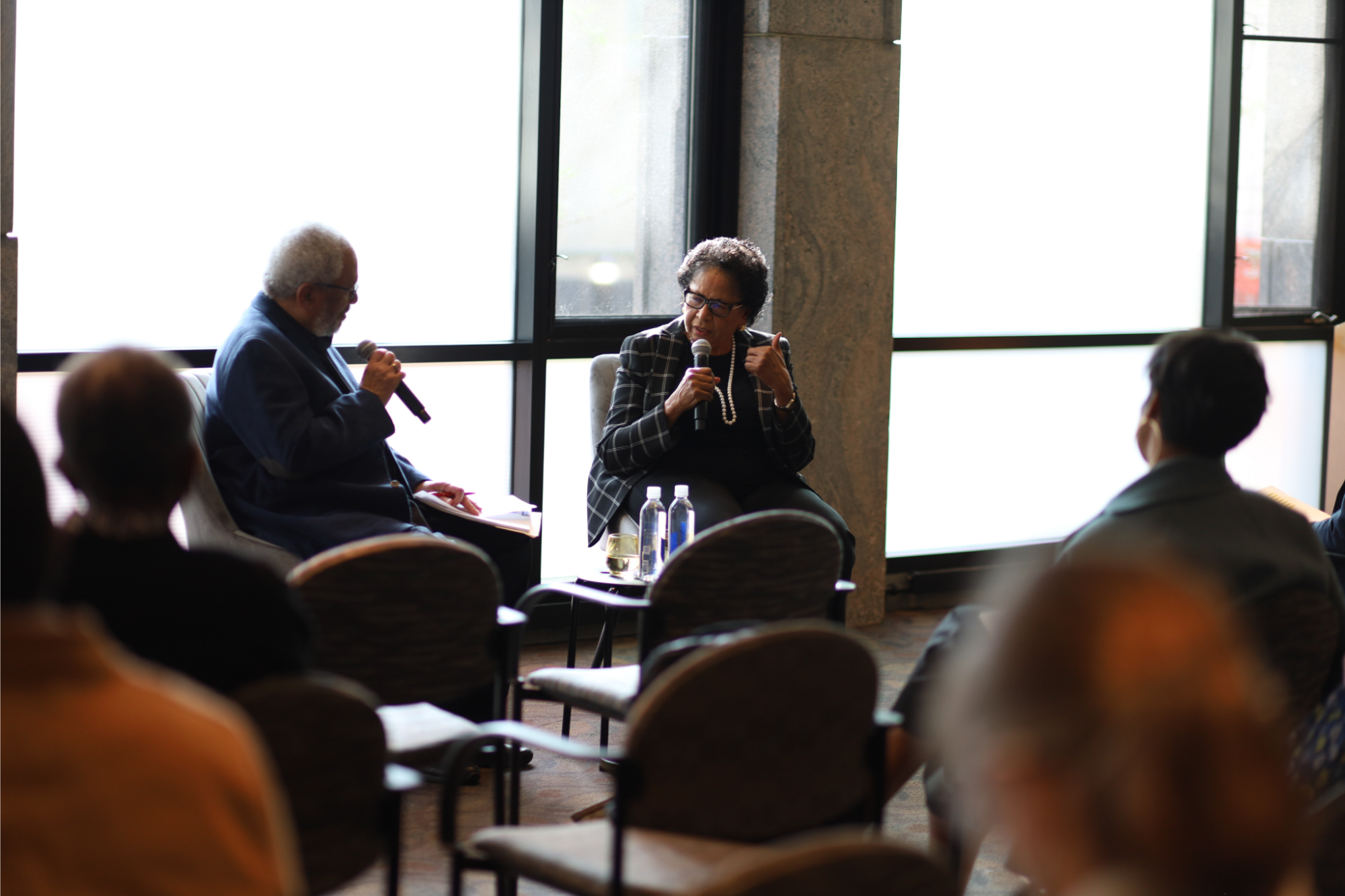 Two people seated having a conversation in front of an audience