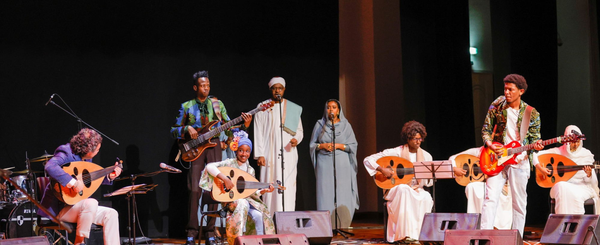 Group performing on a stage with a variety of string instruments and vocalists.