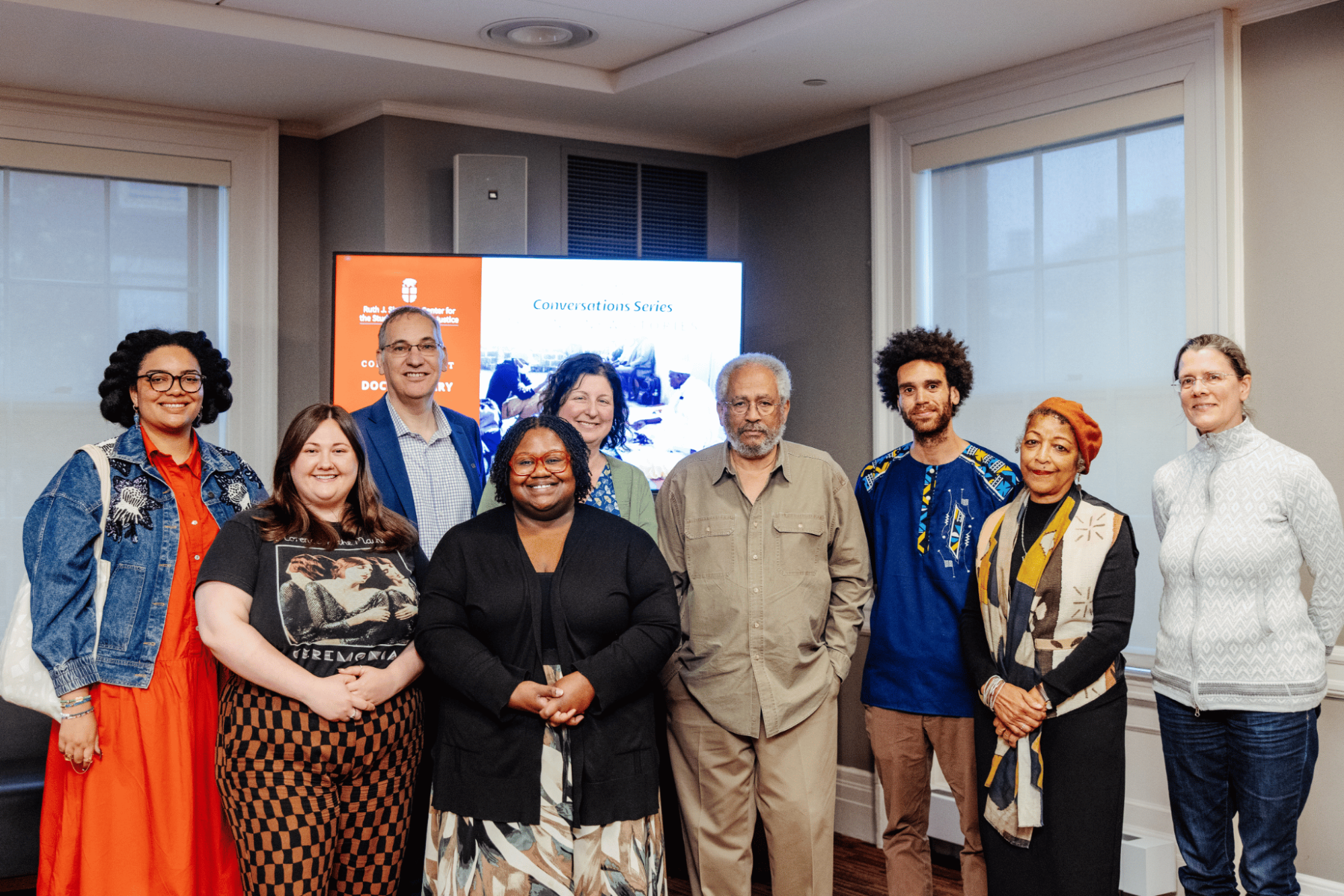 Group of people standind and smiling in front of a screen presentation.