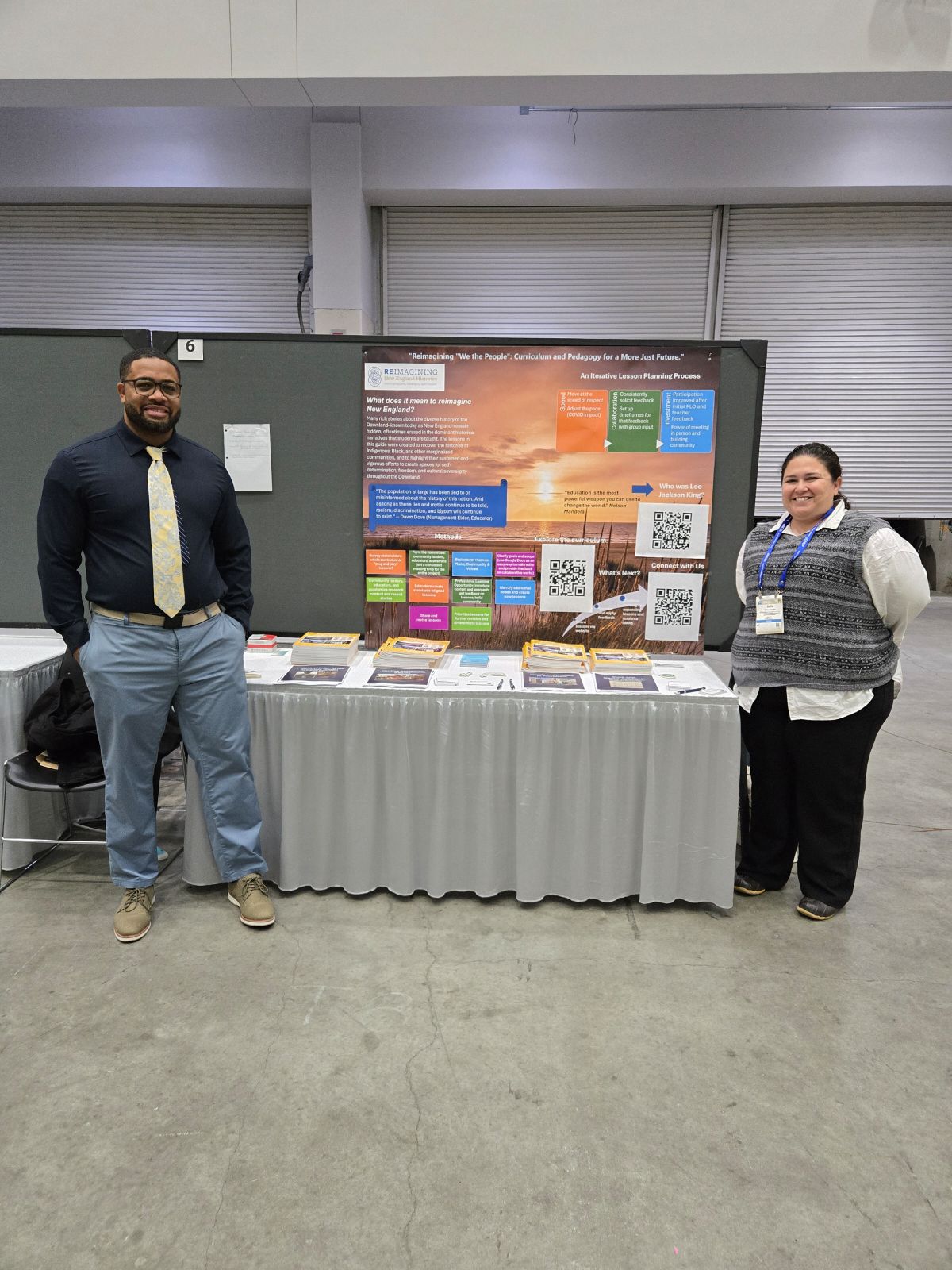 Two people standing in front of a table top presentation and table of books.