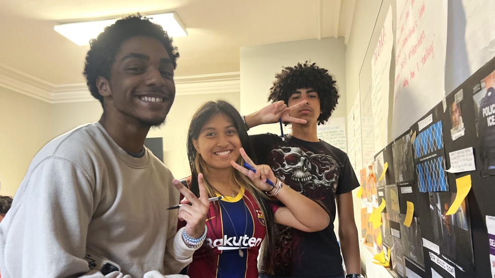 Three students standing and smiling while holding up peace signs. 