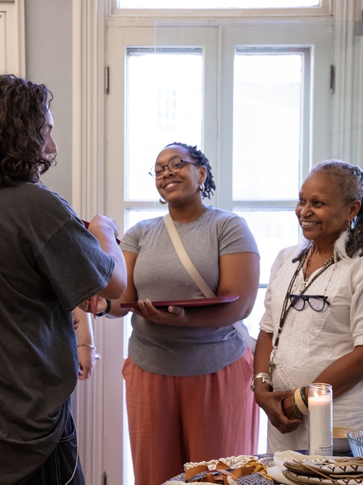 Two people face the camera smiling as a young person accepts a certificate and looks at the community altar