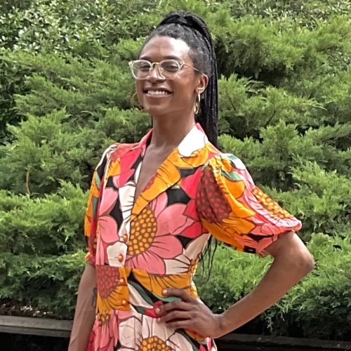 A woman smiling at the camera and wearing a pink and yellow floral dress