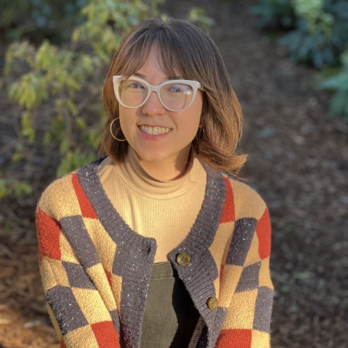 A woman smiling at the camera with white-rimmed glasses and a cozy checked sweater