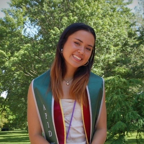 A woman wearing graduation stoles smiles at the camera