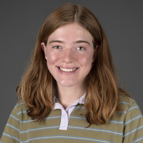 A woman smiling at the camera in front of a grey background