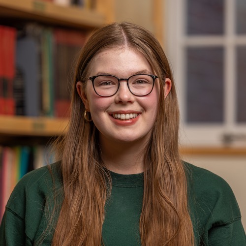 A woman smiling at the camera in front of a bookshelf