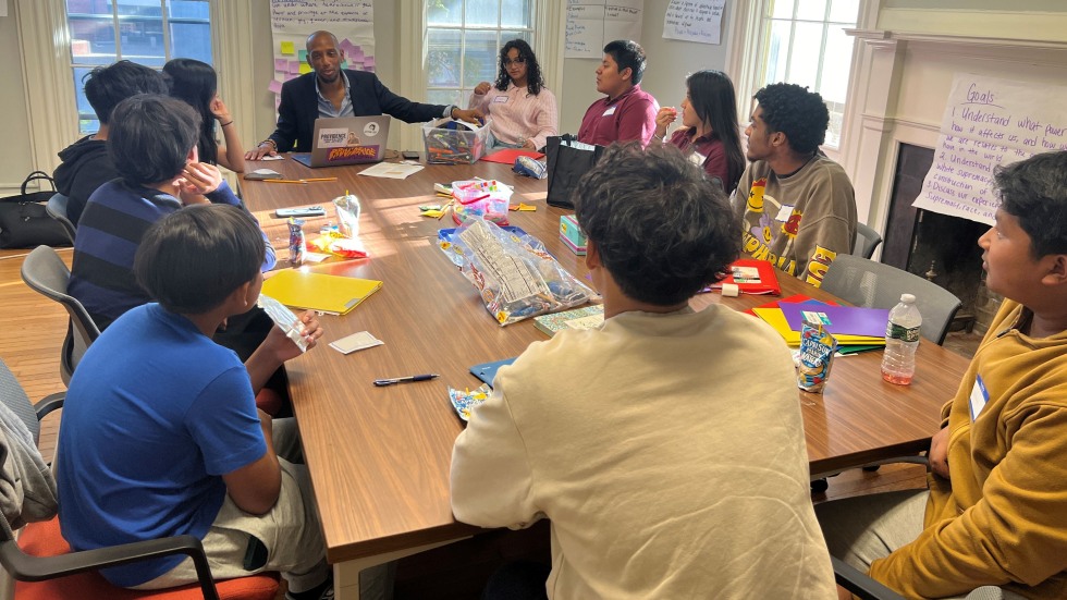 Several students and an educator site around a conference table with educational activity materials in front of them.