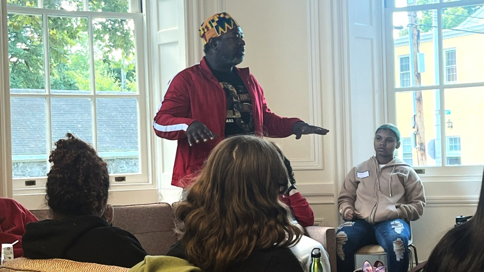 A man standing while speaking to students seated on couches