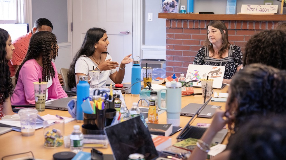 A student talks with the presenter while other students around the table listen