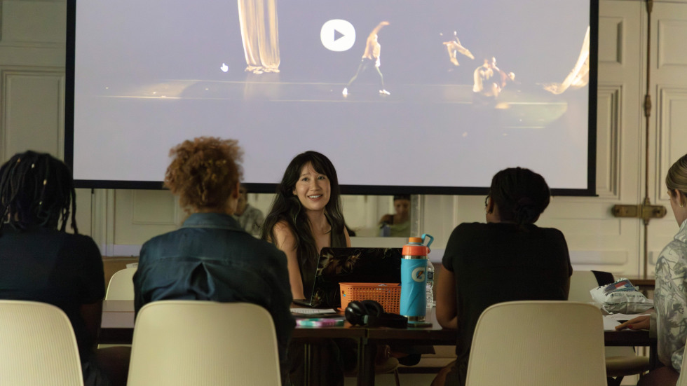 Woman presenting a video to a table of students.
