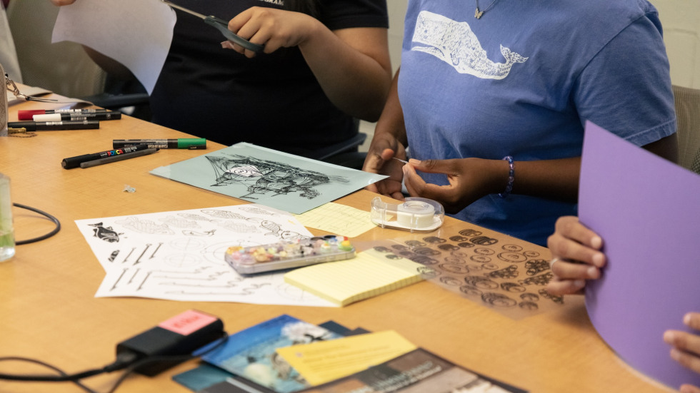 Three people work on their collages with markers and materials spread out on the table in front of them.