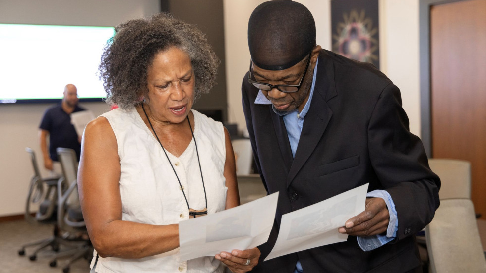 Two people stand side by side with serious faces, examining papers they are holding